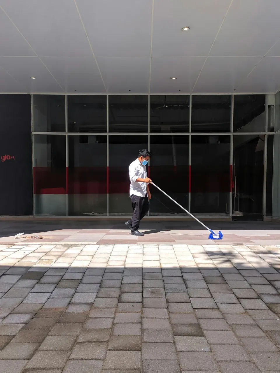Agent de propreté nettoyant un sol pavé devant une devanture commerciale