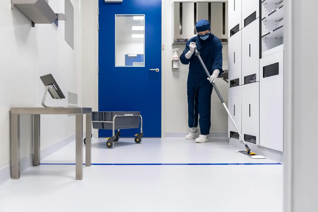 Agent en combinaison stérile lavant le sol d'une salle blanche en environnement de santé