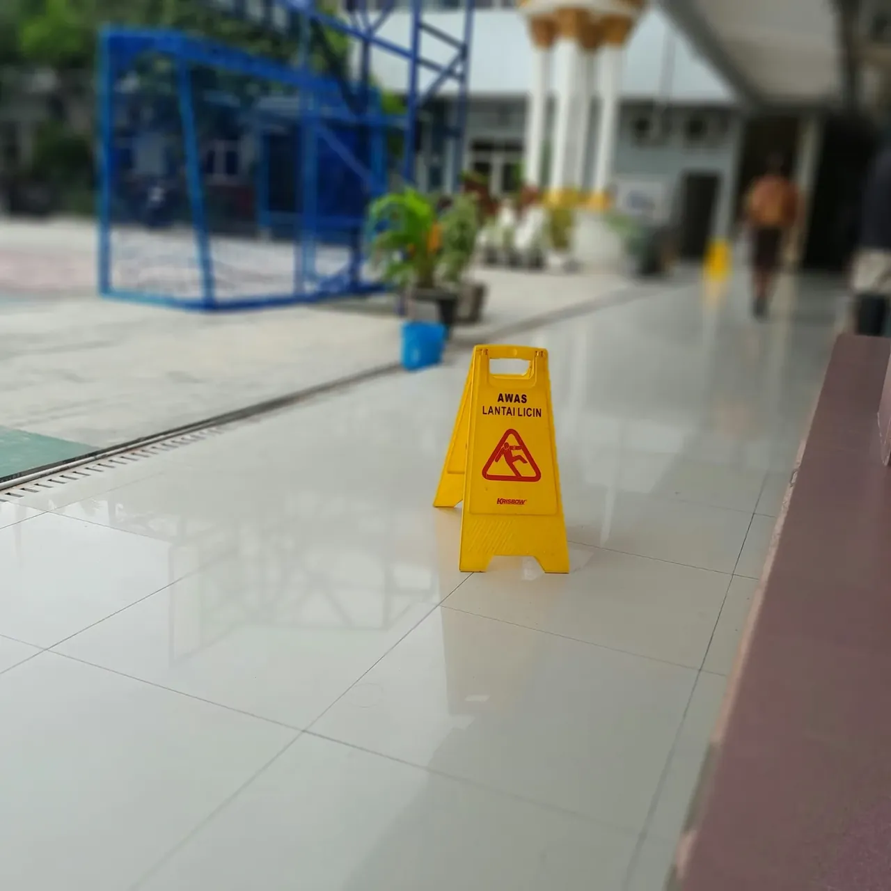 Panneau de signalisation sol glissant posé sur un carrelage brillant après nettoyage