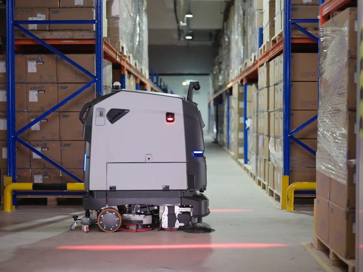 The PUDU BG1 in a warehouse aisle between racks
