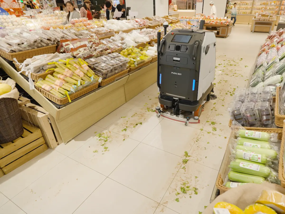 The PUDU BG1 dealing with dry debris and a spilled liquid in a supermarket aisle